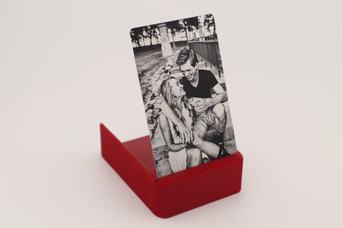A red rectangular display stand holding a vertical black-and-white photo print of a couple, photographed on a clean light gray background.