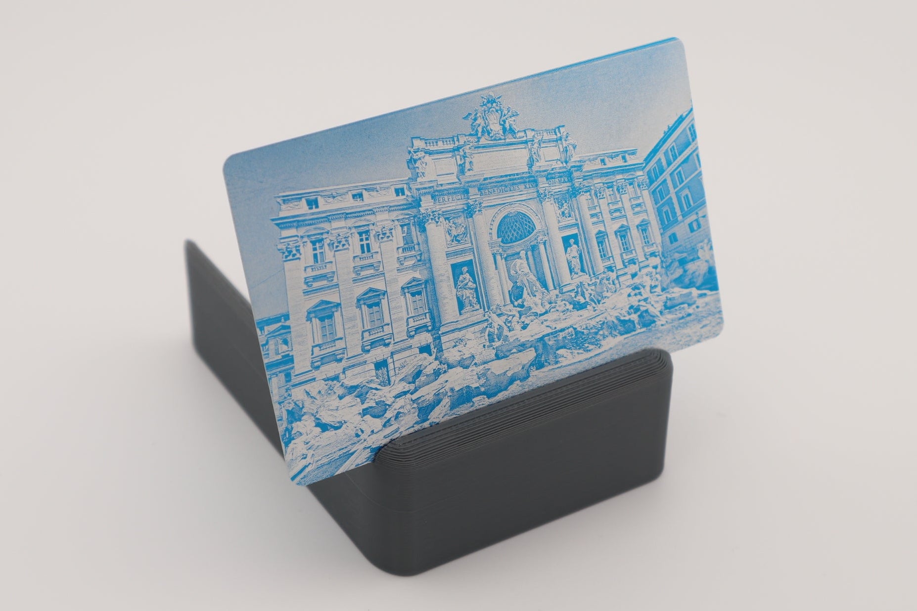 A rectangular engraved card with a blue architectural building design, displayed upright on a black stand against a plain light background.